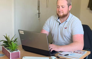 man working on laptop in office with plant and paperwork