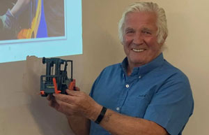 a man in a blue shirt smiling while holding a model forklift