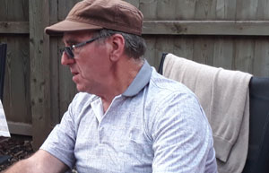 man sitting outdoors wearing a cap and glasses